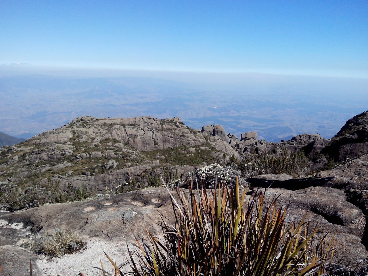 Cume rochoso do Morro do Couto em primeiro plano, com o vale ao fundo sob céu azul