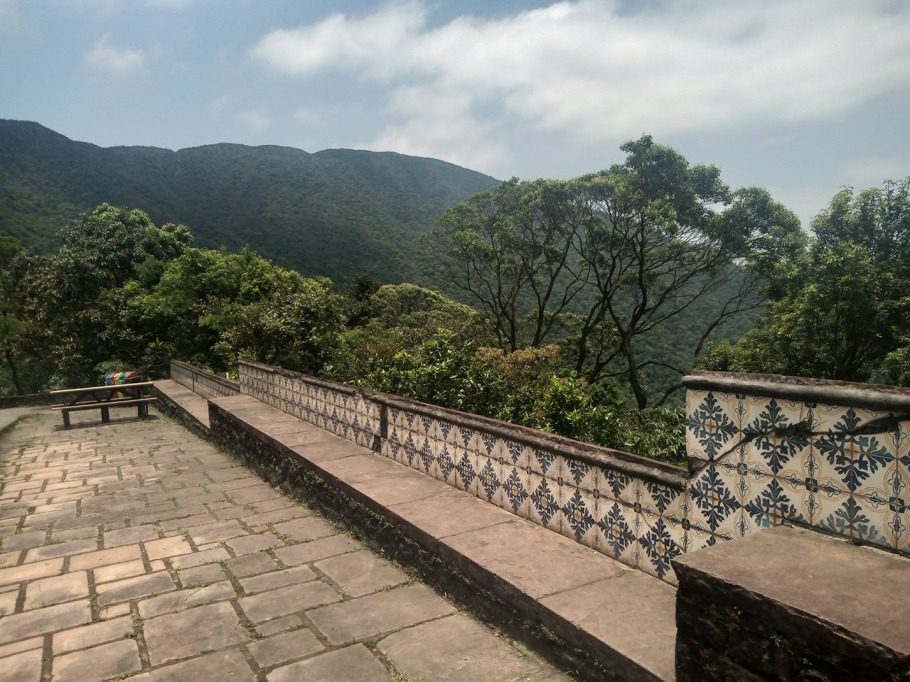 Terraço de pedra com mureta de azulejos no mirante do Rancho da Maioridade, com a serra coberta de mata ao fundo