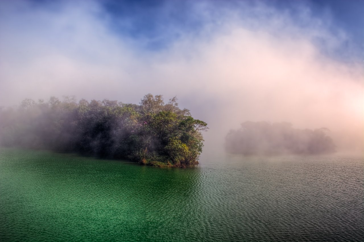 Ilhas de vegetação sobre a água esverdeada do Reservatório Rio das Pedras, envoltas em neblina