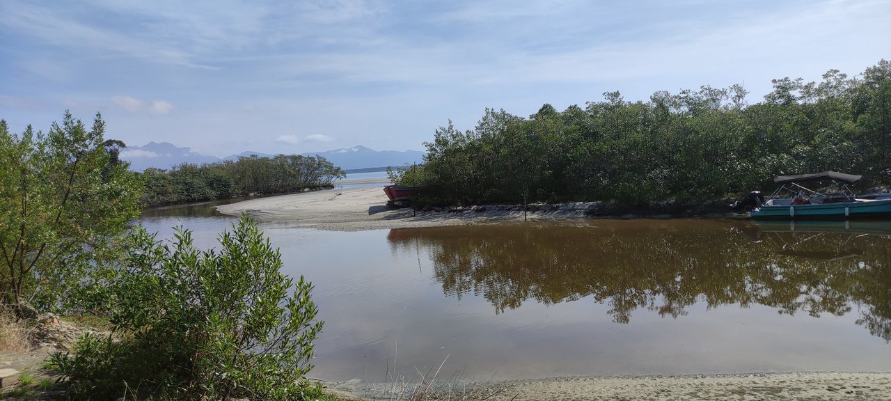 Rio Perequê de águas calmas com mangue nas margens, um barco à direita e a serra ao fundo