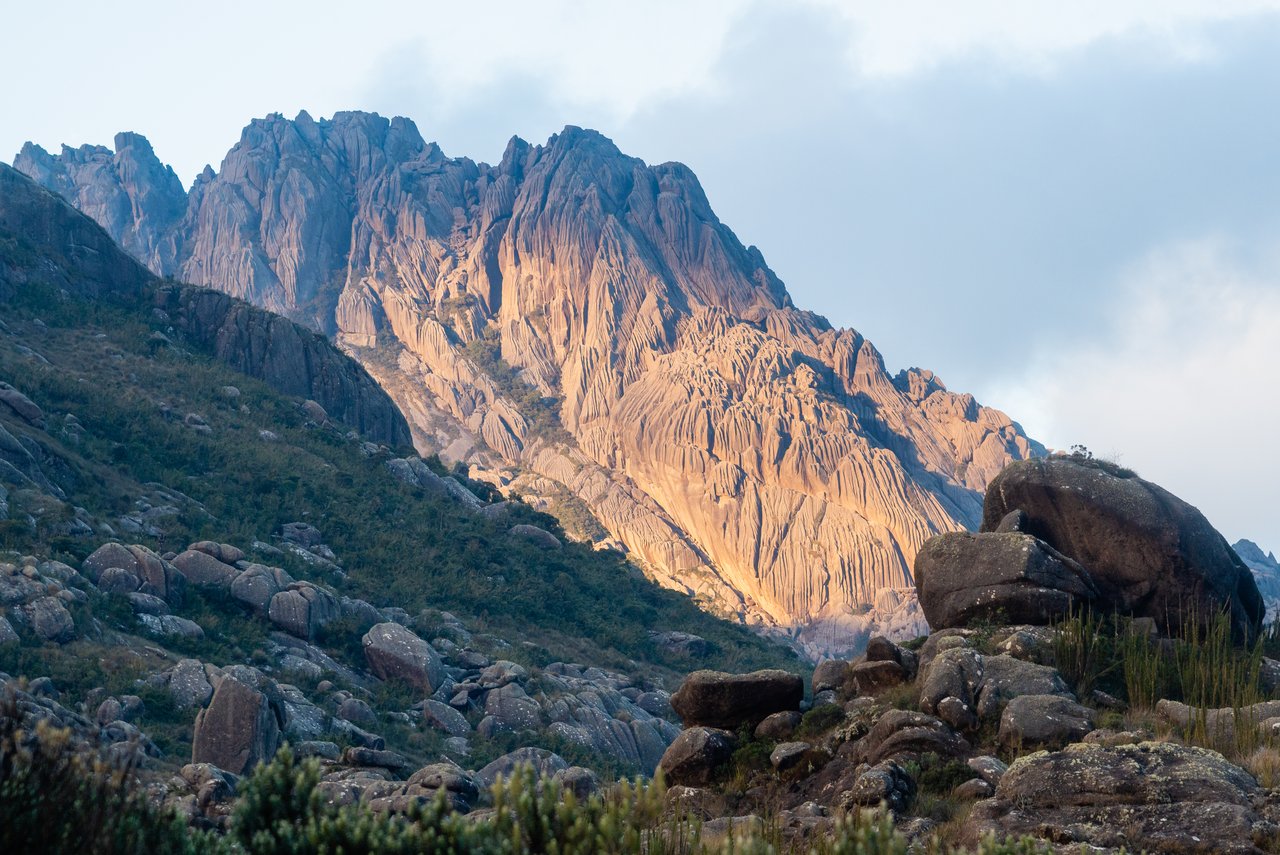 Paredões rochosos do Parque Nacional do Itatiaia iluminados pelo sol, com blocos de pedra e vegetação de altitude em primeiro plano