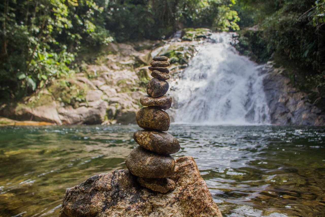 Cachoeira do Ribeirão de Itu ao fundo e, em primeiro plano, uma pilha de pedras equilibradas sobre uma rocha no poço