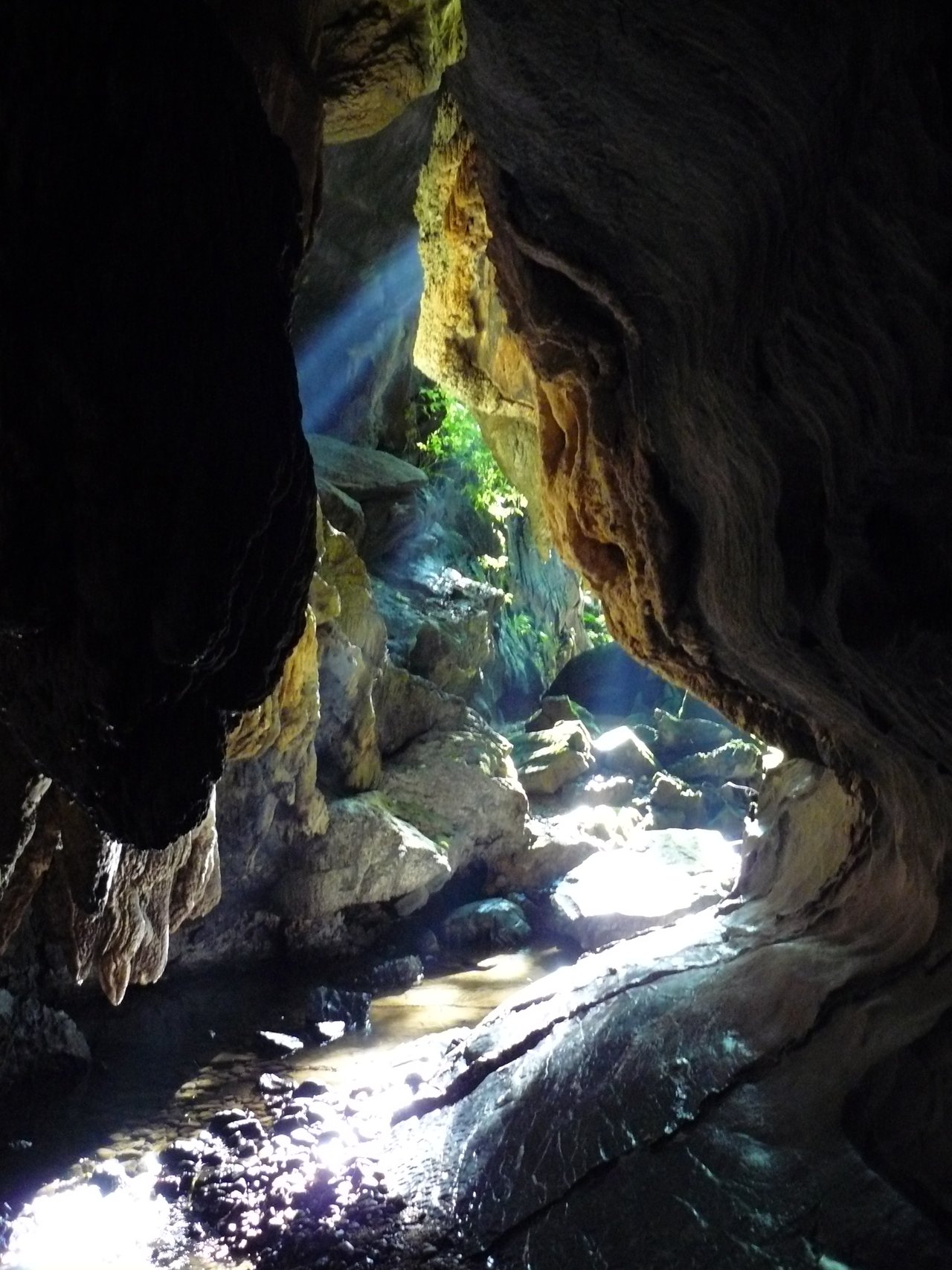 Interior da Caverna Chapéu Mirim, com um feixe de luz entrando pela fenda e o chão úmido refletindo