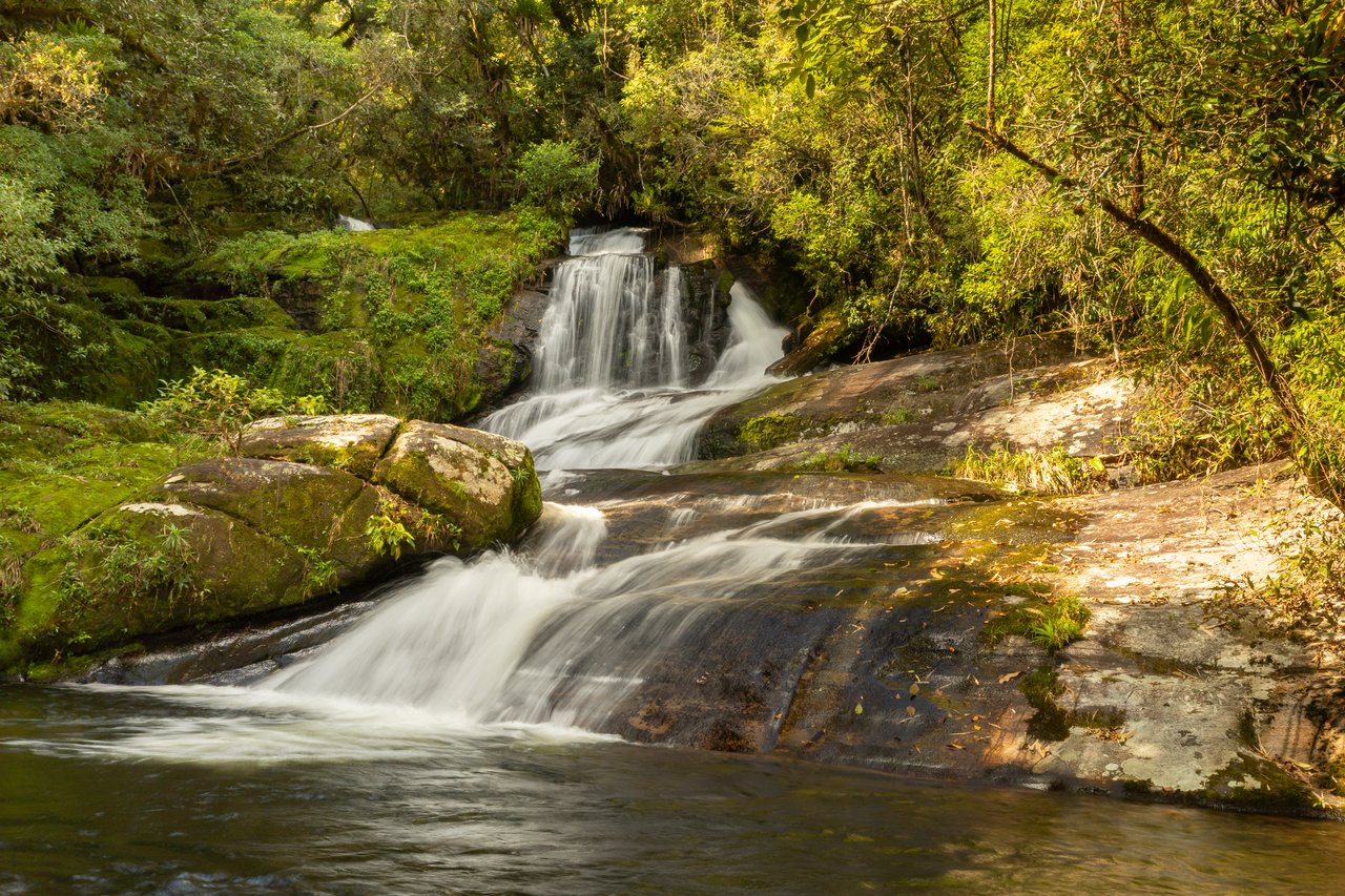 Cachoeira em degraus escorrendo sobre lajes de pedra cobertas de musgo, na mata do Núcleo Cunha