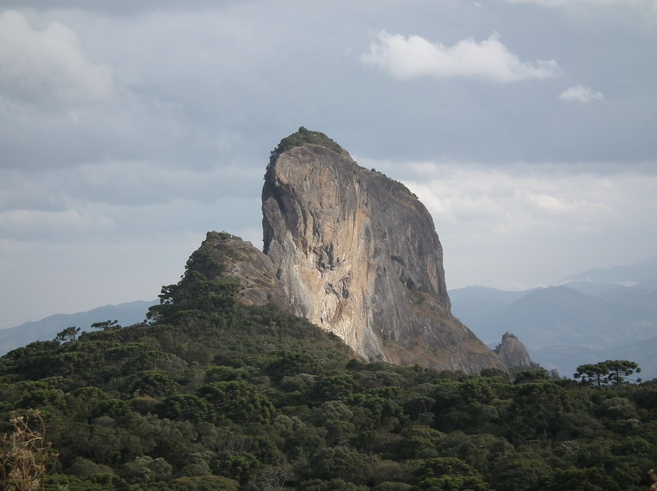 Pedra do Baú vista de longe, com sua parede de rocha erguendo-se acima da mata, sob céu nublado